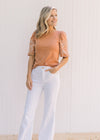 Model wearing white wide leg pants with a burnt orange top with a cream floral embroidery on sleeve.