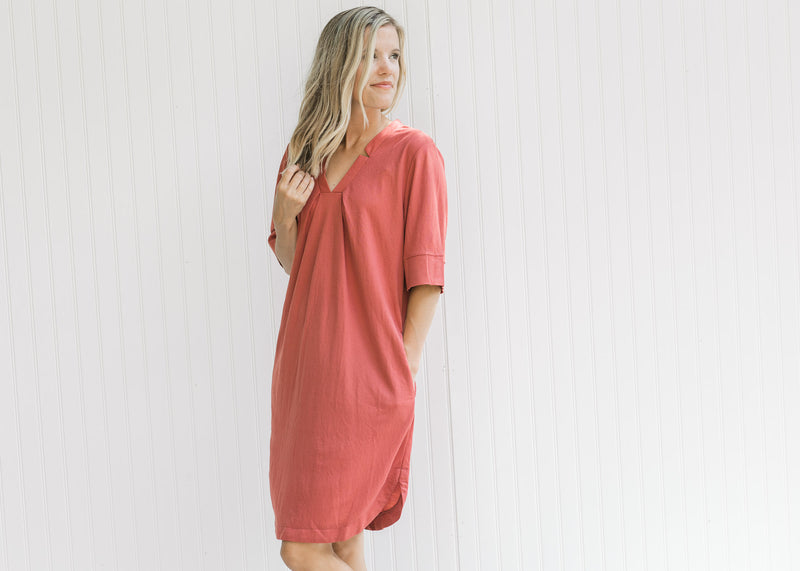 Model wearing a burgundy above the knee dress with a notch v-neck, short sleeves and pockets. 