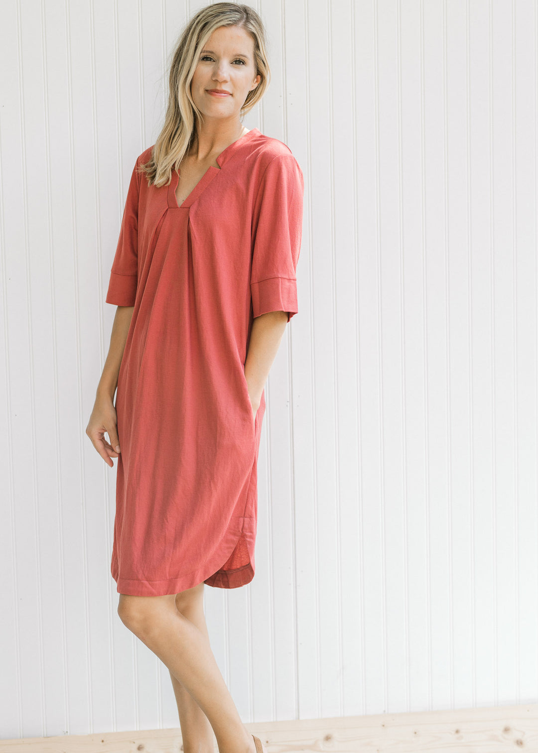 Model wearing a burgundy dress with a notch v-neck, short sleeves and pockets. 