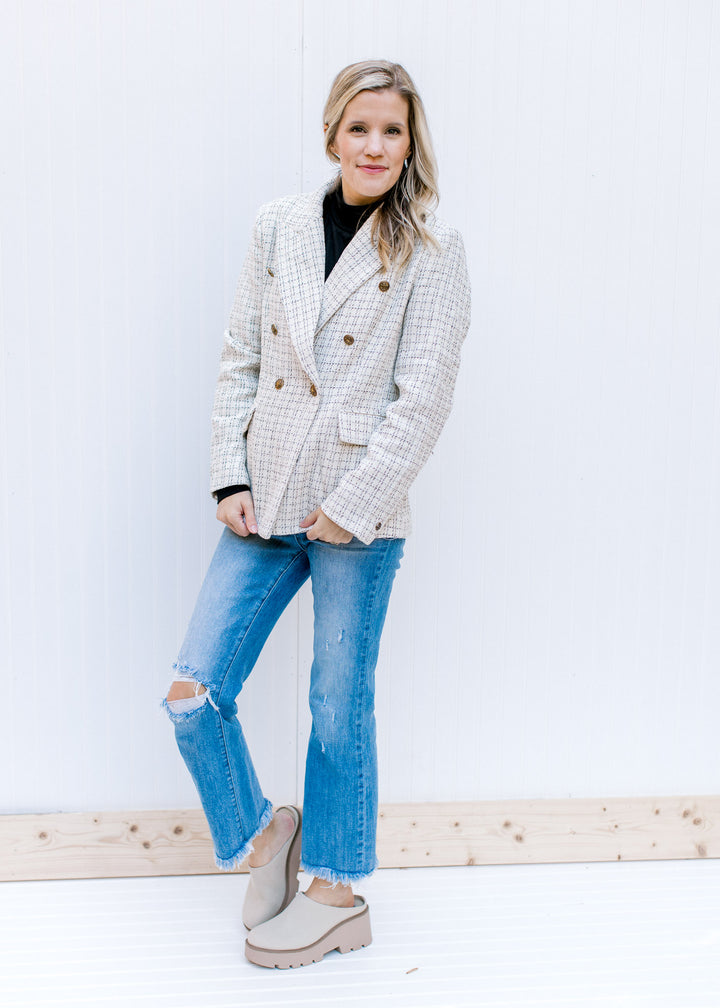 Model wearing jeans and a cream plaid blazer with gold double breasted buttons and flap pockets.