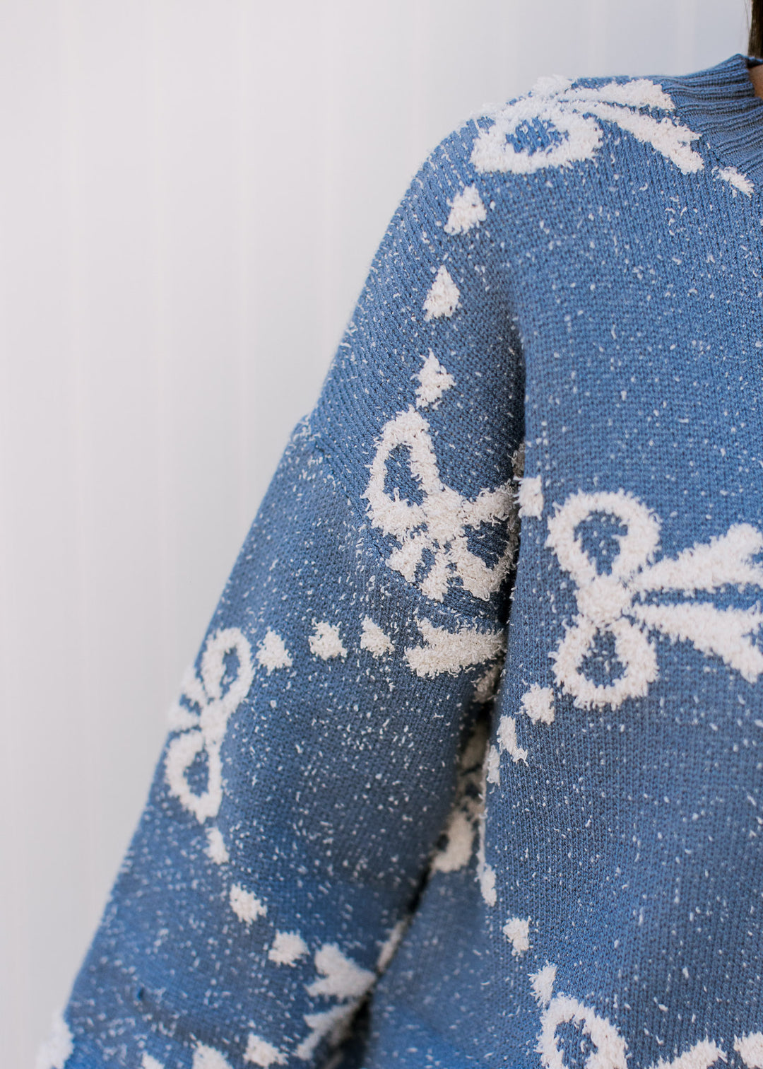 Close up of texturing, cream ribbons and dots on a dusty blue sweater with long sleeves. 