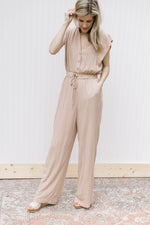 Model wearing a beige jumpsuit with button bodice, elastic waist with tie and wide legs.