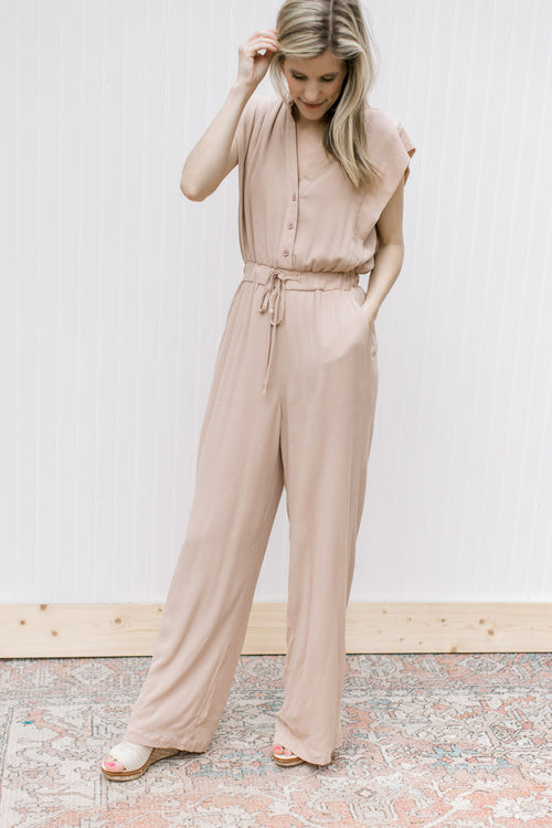 Model wearing a beige jumpsuit with button bodice, elastic waist with tie and wide legs.