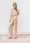 Model wearing heels and a beige jumpsuit with button bodice, elastic waist with tie and wide legs.