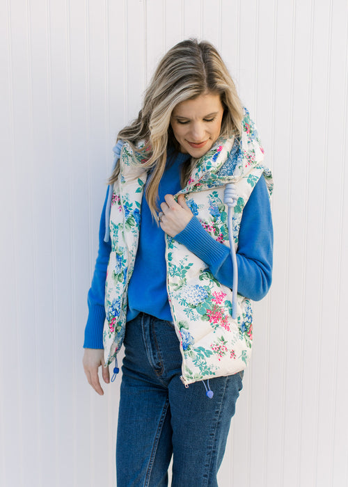 Model wearing a white puffer vest with blue, pink and green floral, hoodie and zipper closure. 