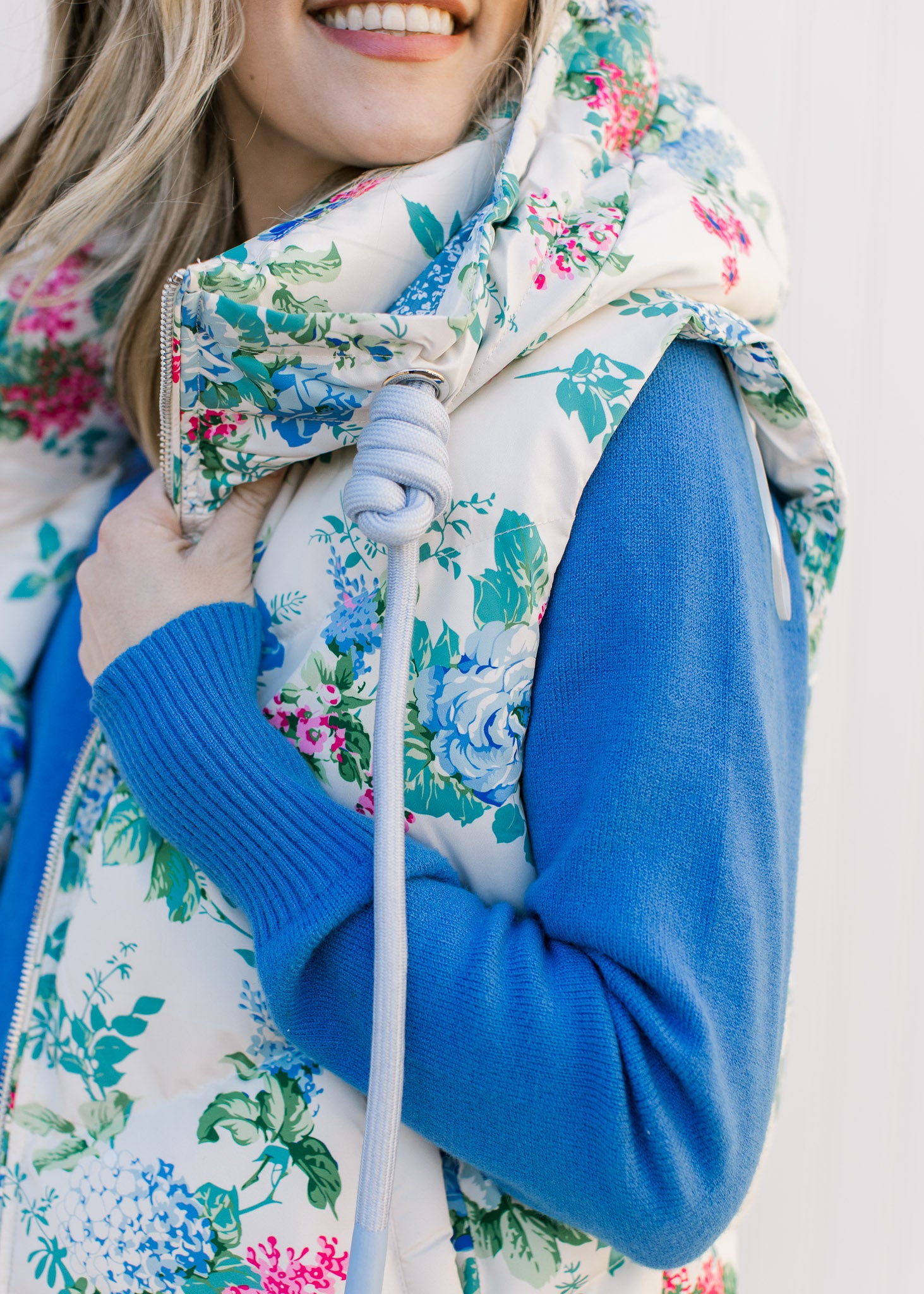 Close up of the rope tie from the hood of a white vest with a pink, blue and green floral pattern 