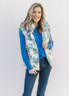 Model wearing a blue top with a white puffer vest with blue, pink and green floral design. 