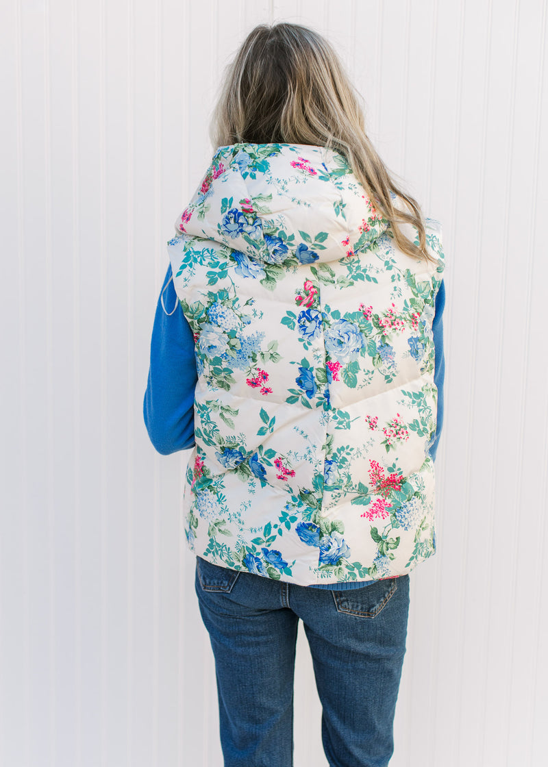 Back view of Model wearing a white puffer vest with blue, pink and green floral design and a hoodie.