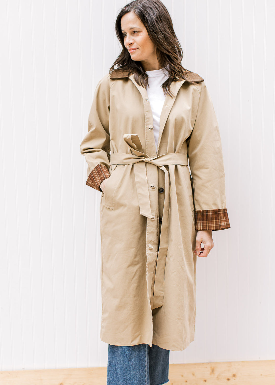 Model wearing a camel jacket with buttons, brown corduroy collar and long sleeves with plaid cuffs. 