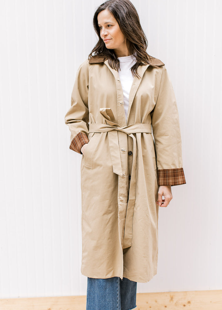 Model wearing a camel jacket with buttons, brown corduroy collar and long sleeves with plaid cuffs. 