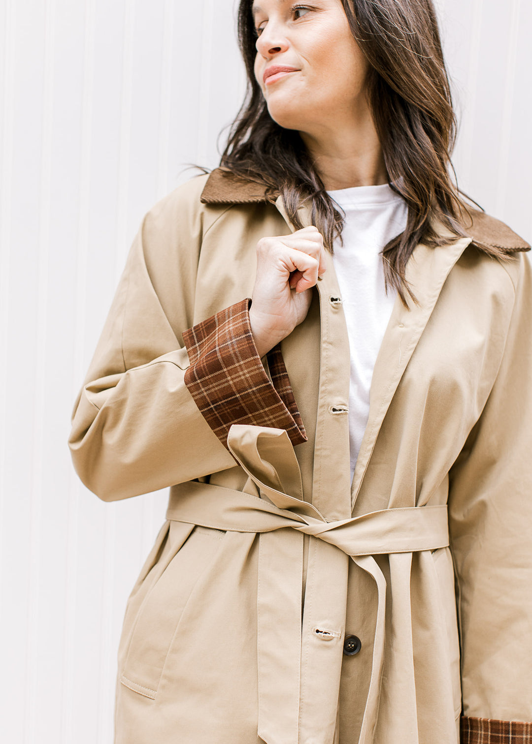Close up of brown corduroy flap collar and plaid cuff on a camel colored jacket with a tie waist. 