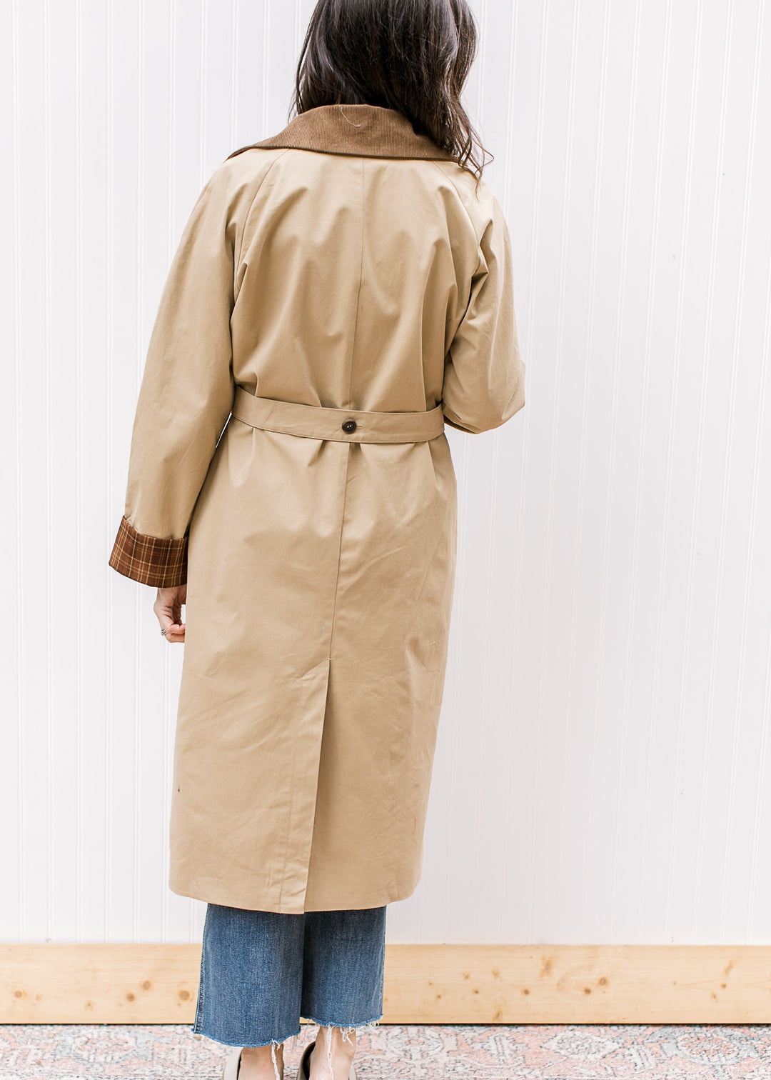 Back view of Model wearing a camel jacket with brown collar and long sleeves with plaid cuffs. 