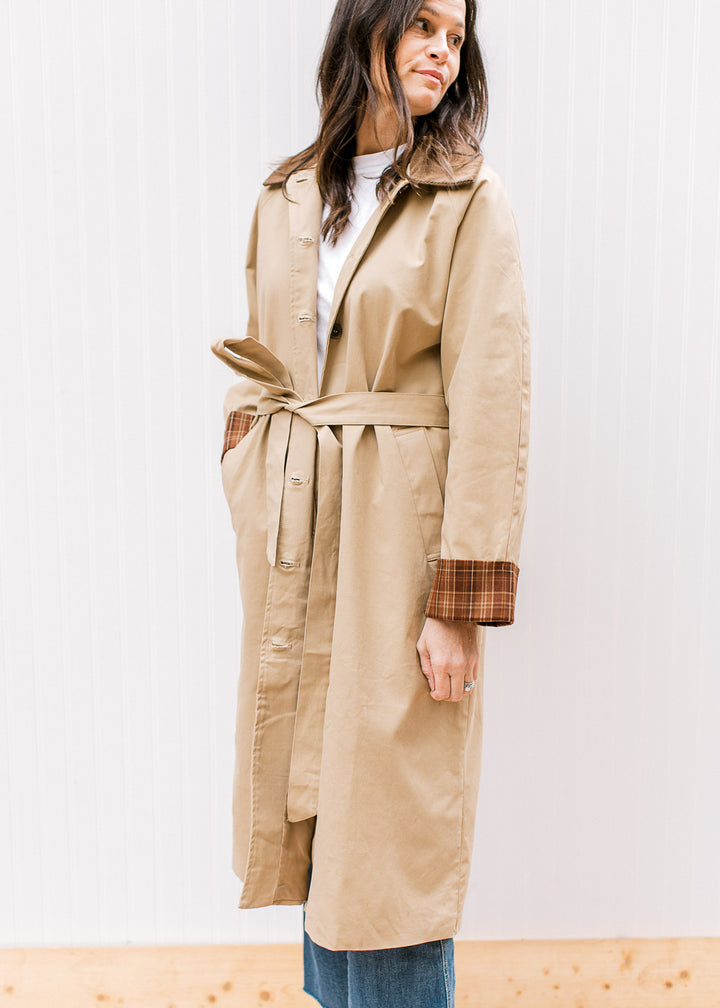 Model wearing a camel colored trench coat with button front, tie at waist and pockets. 