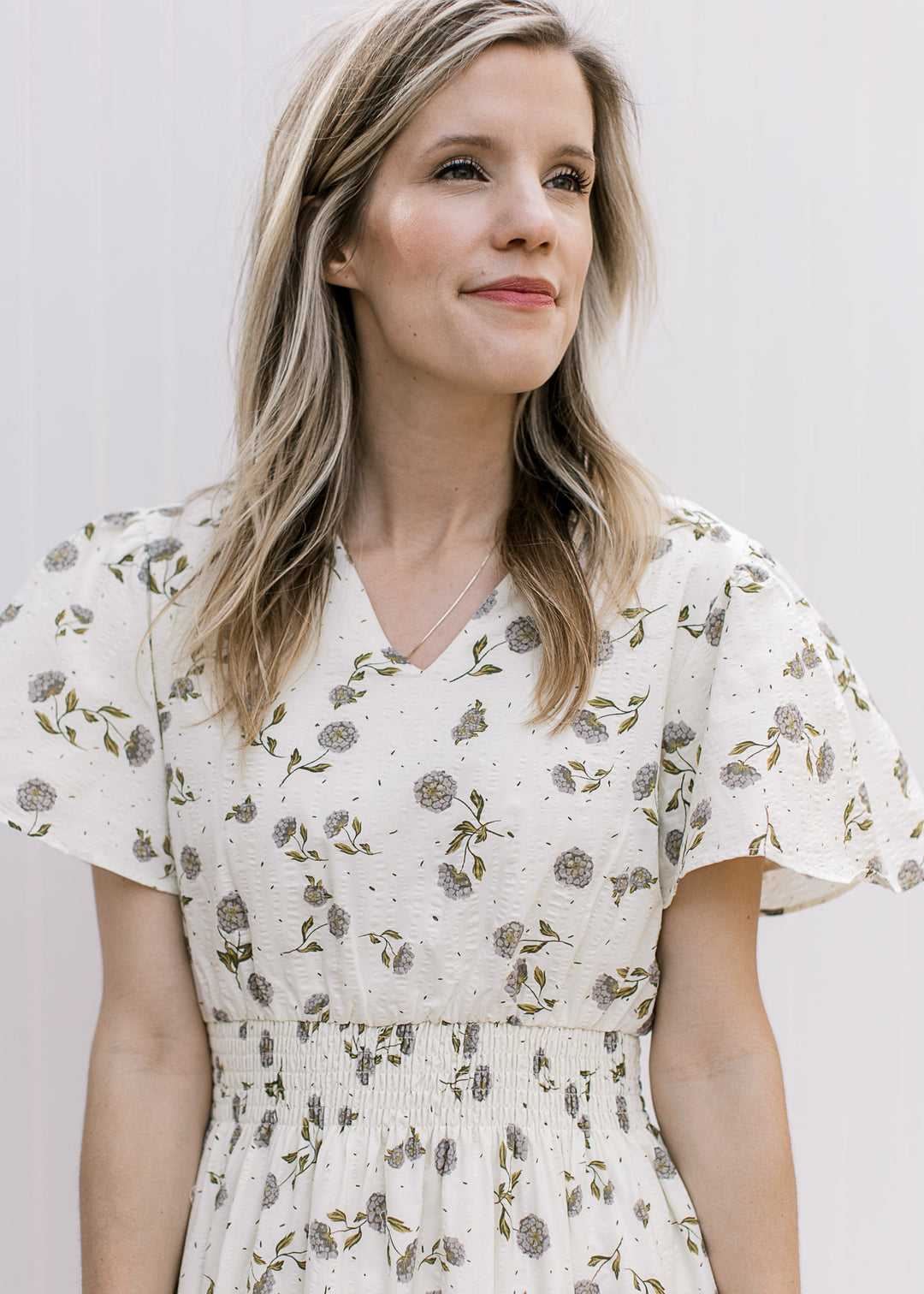 Close up of flutter short sleeves, v-neck and elastic waist on a cream maxi with hydrangeas. 