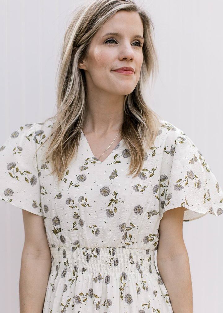 Close up of flutter short sleeves, v-neck and elastic waist on a cream maxi with hydrangeas. 