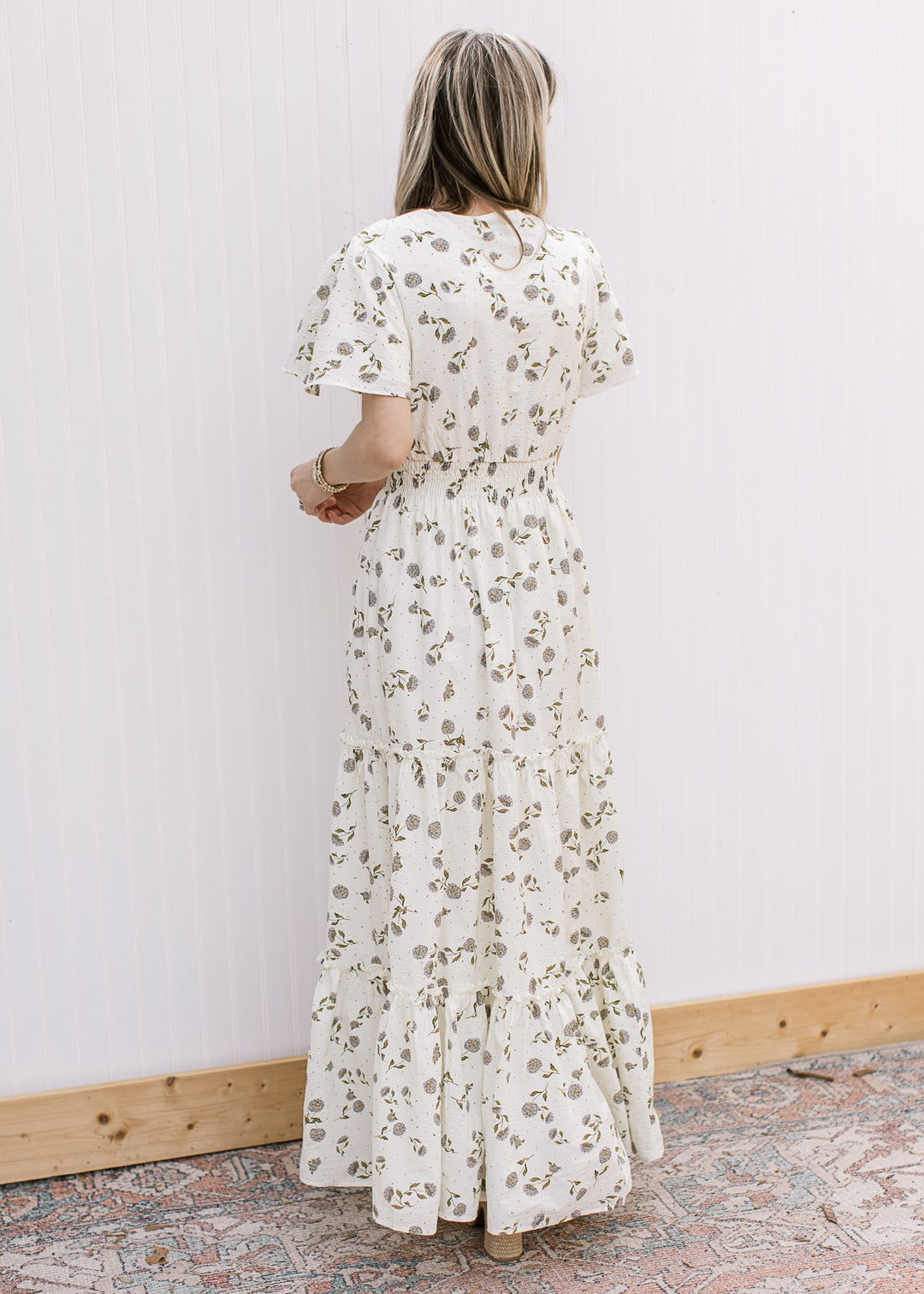 Back view of Model wearing a cream maxi with hydrangeas, flutter short sleeves and elastic waist.