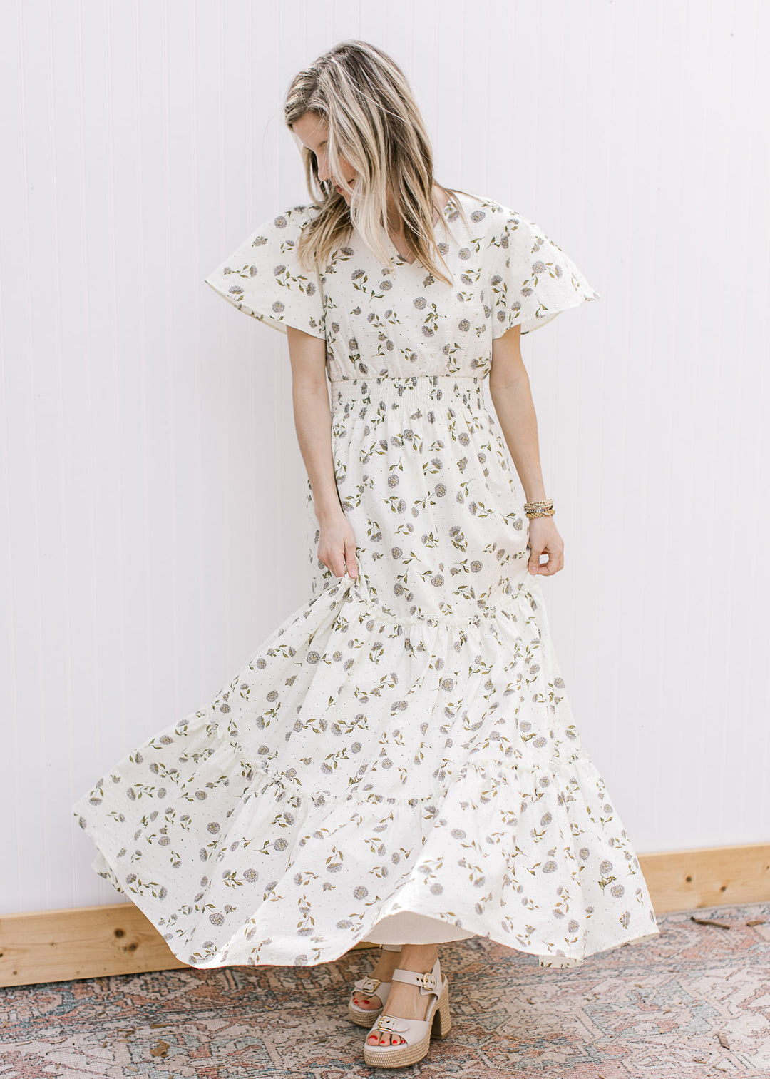 Model wearing heels and a cream v-neck maxi with hydrangeas, short sleeves and elastic waist.