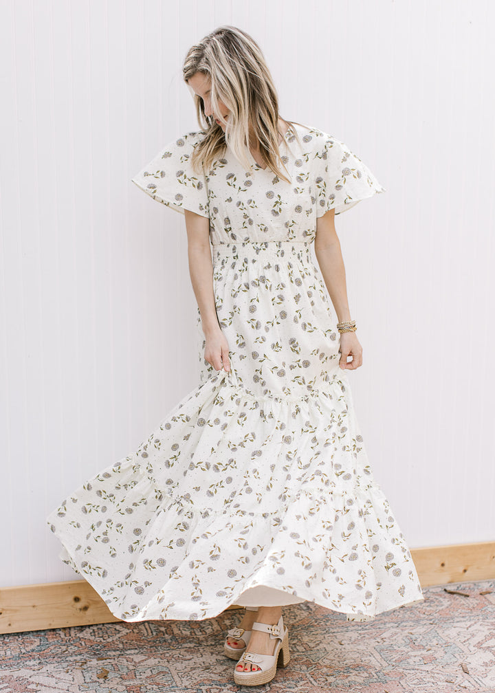 Model wearing heels and a cream v-neck maxi with hydrangeas, short sleeves and elastic waist.