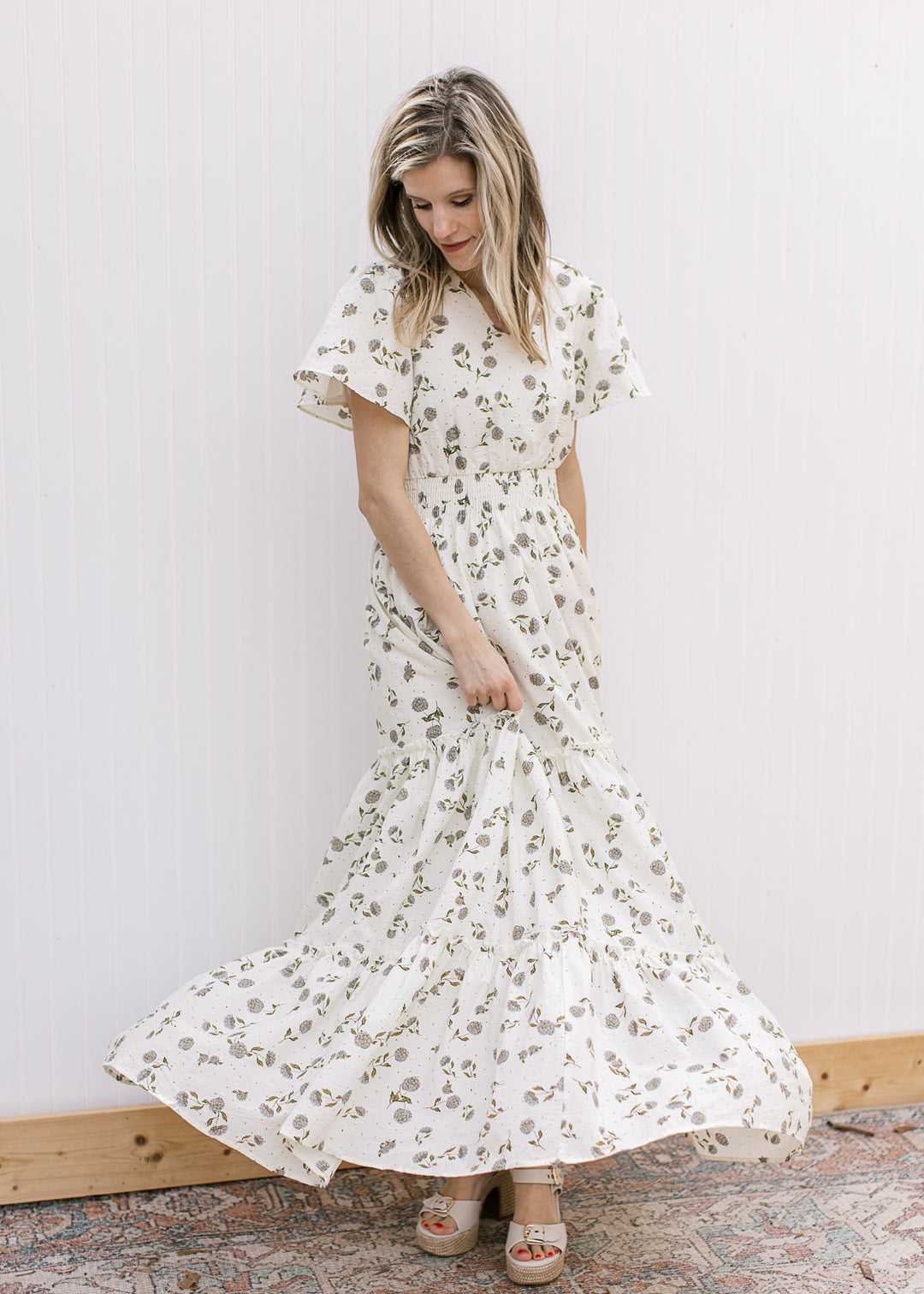 Model wearing a cream maxi with hydrangea print, tiers, flutter short sleeves and elastic waist.