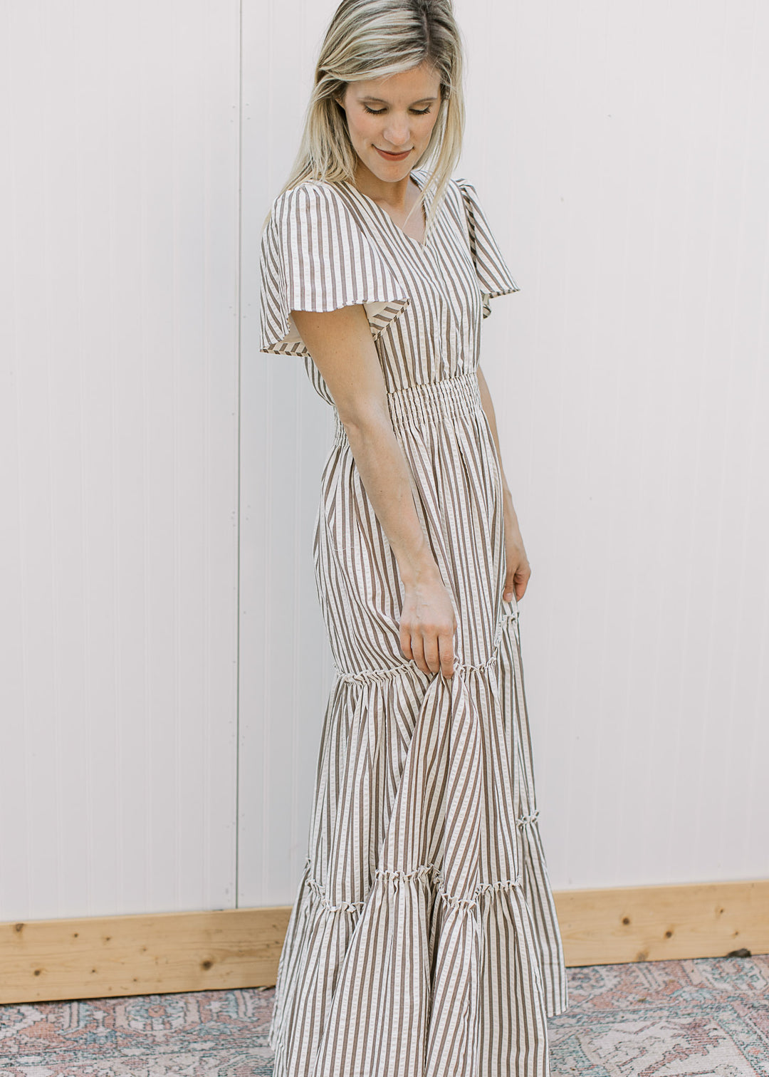 Model wearing a cream maxi with brown vertical stripes, v-neck, short sleeves and elastic waist.