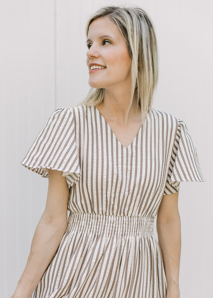 Model wearing a cream maxi with brown stripes, v-neck, flutter short sleeves and elastic waist.