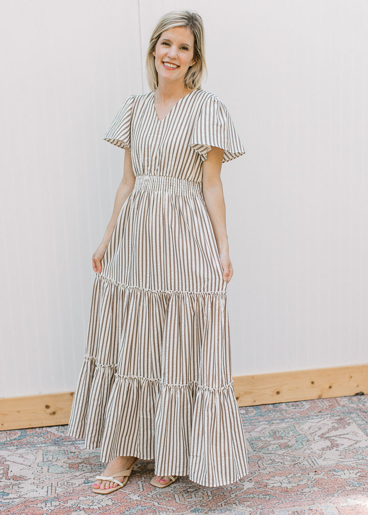 Model wearing a cream maxi with brown stripes, v-neck, short sleeves and tiered skirt. 