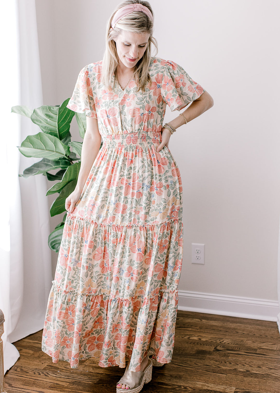 Model wearing a beige maxi with pink, floral, flutter short sleeves, v-neck and elastic waist.
