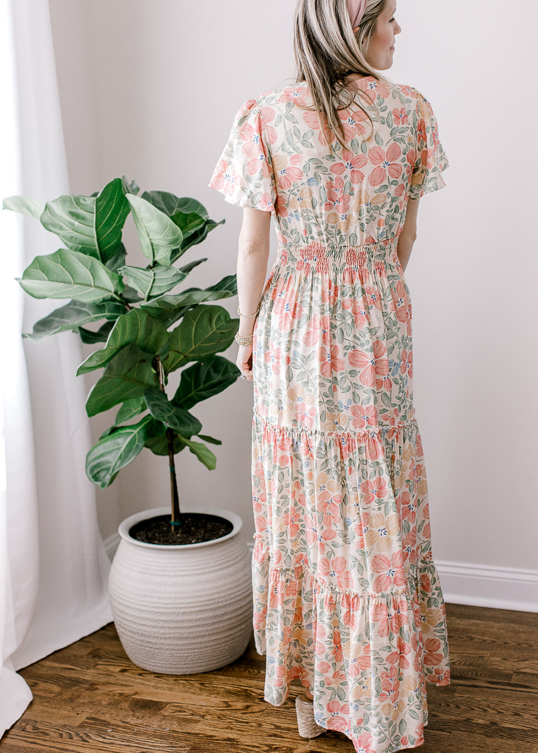 Back view of Model wearing a beige maxi with pink, floral, short sleeves, v-neck and elastic waist.