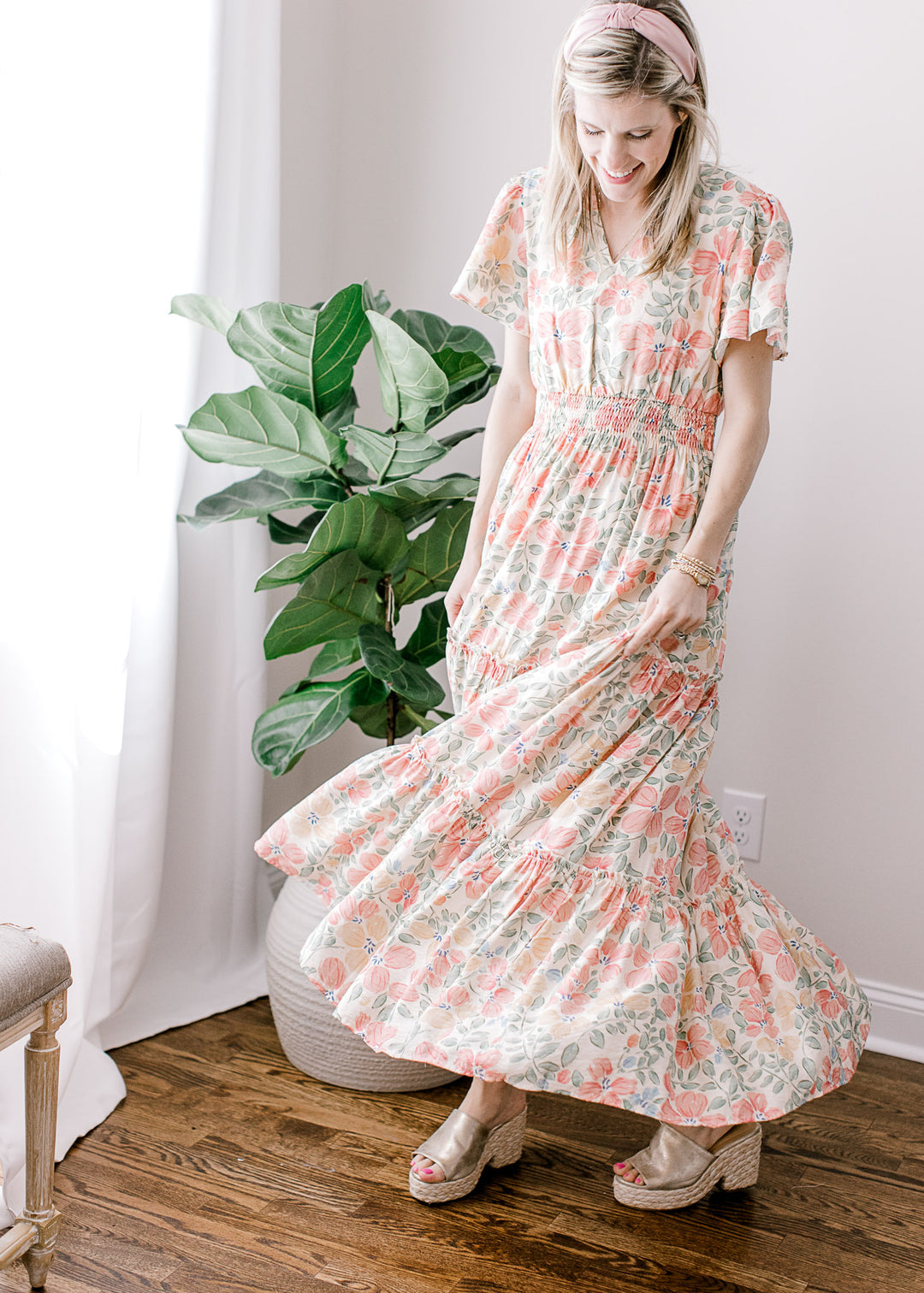 Model twirling in a beige maxi with pink, floral, flutter short sleeves, v-neck and elastic waist.