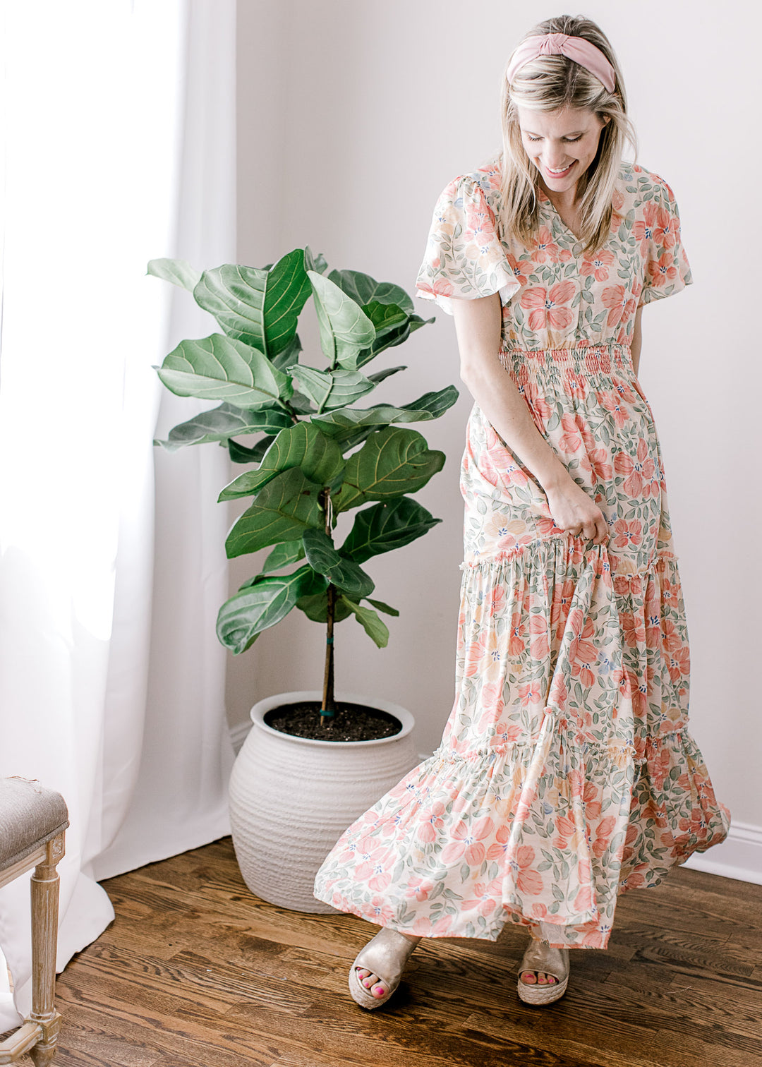 Model wearing a beige maxi with pink, floral, flutter short sleeves, v-neck and tiered skirt. 