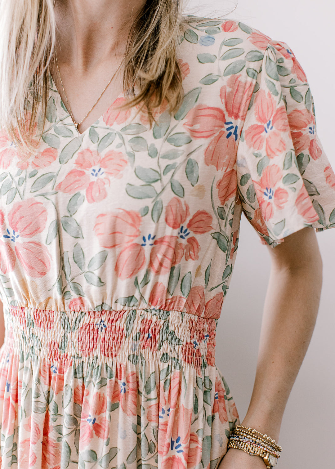 Close up of v-neck, flutter sleeves and smocked waistband on a cream midi with floral. 