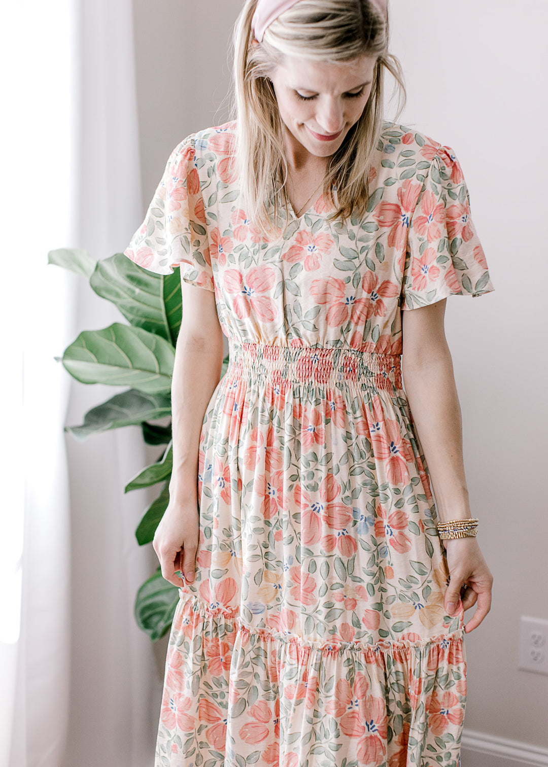 Model wearing a beige maxi with pink, floral and flutter short sleeves with pleated shoulders. 