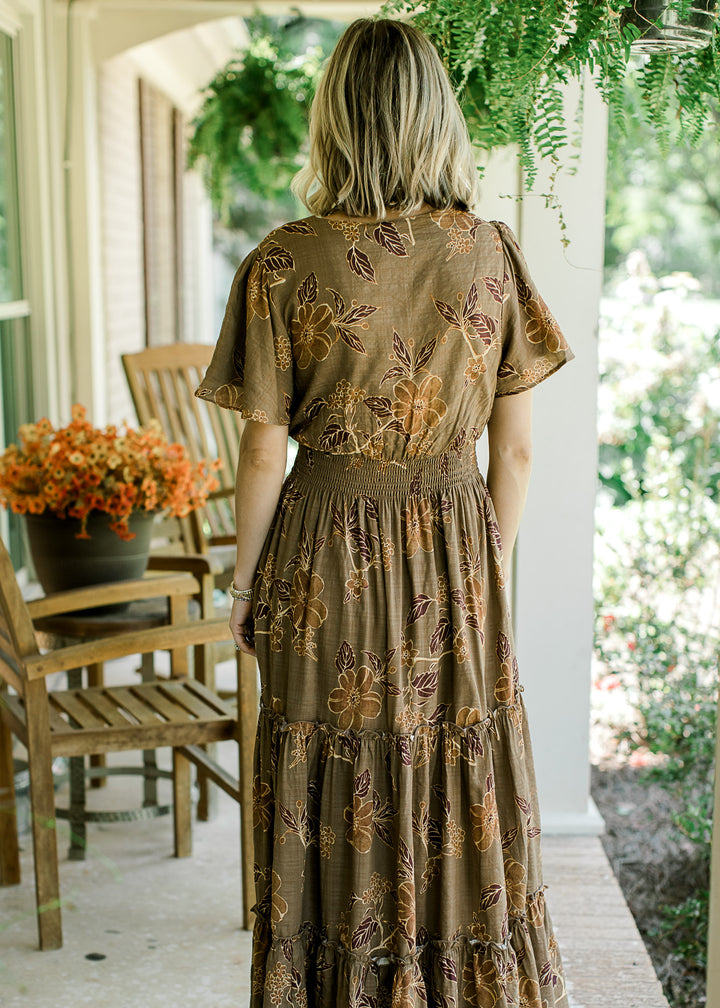 Back view of blonde model wearing floral maxi with gold, brown, and rust pattern.