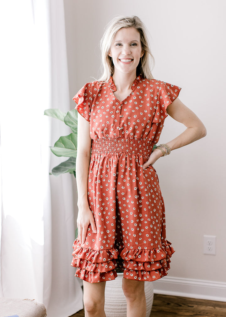 Model wearing a maroon above the knee dress with white floral, v-neck and a smocked waist.