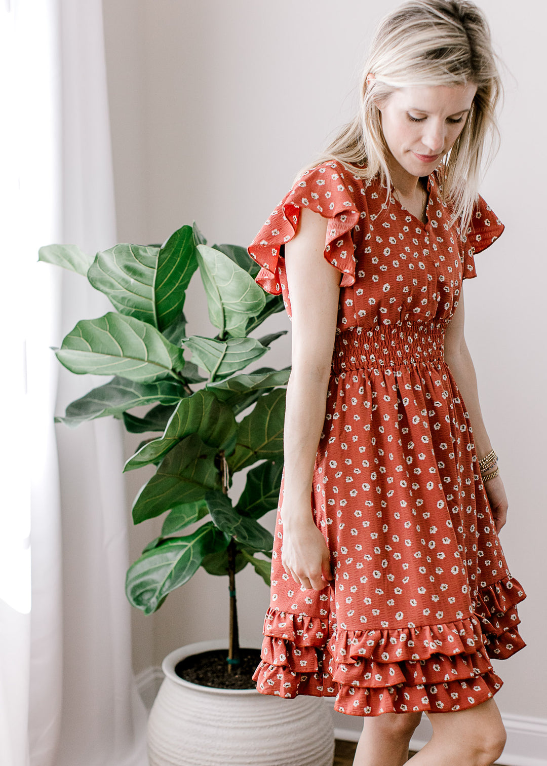 Model wearing a maroon dress with white floral and a ruffle detail at shoulders, neck and hem. 
