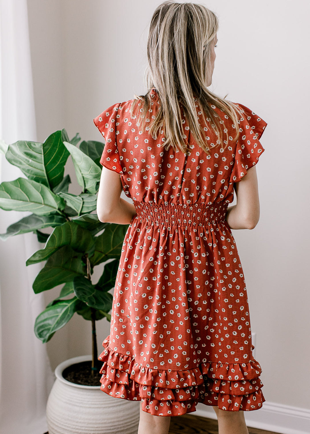 Back view of Model wearing a maroon dress with white floral, v-neck and a smocked waist.