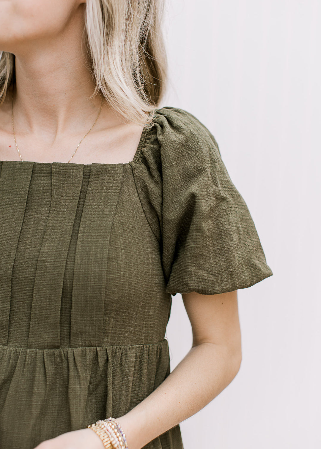 Close up of pleated bust, bubble short sleeves and square neckline on an olive knee length dress.