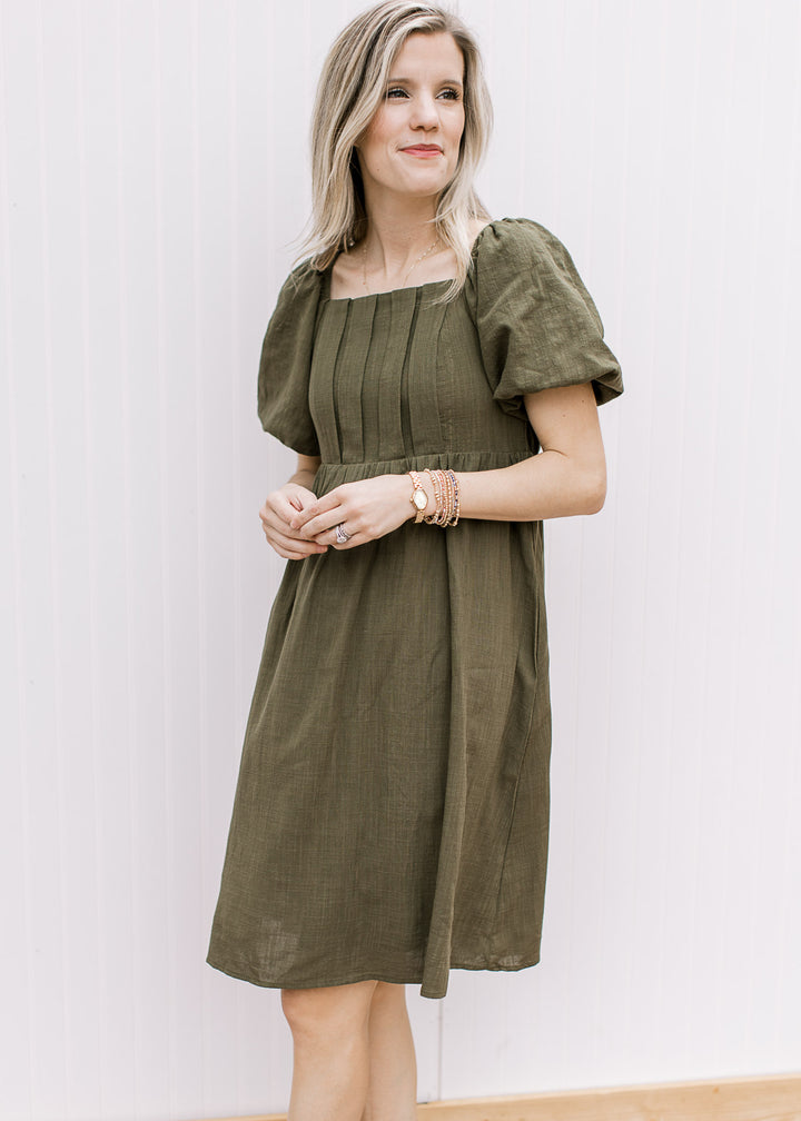 Model wearing an olive knee length dress with a square neck, pleated bust and short sleeves.