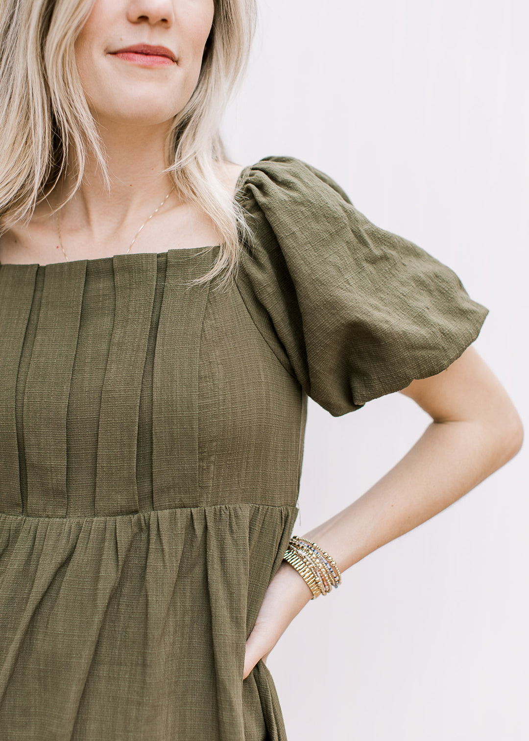 Close up of bubble short sleeves and pleated bust on an olive dress with a square neck. 