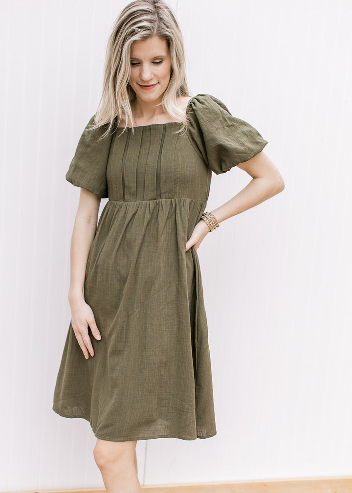 Model wearing a textured olive dress with a square neck, pleated bust and bubble short sleeves.