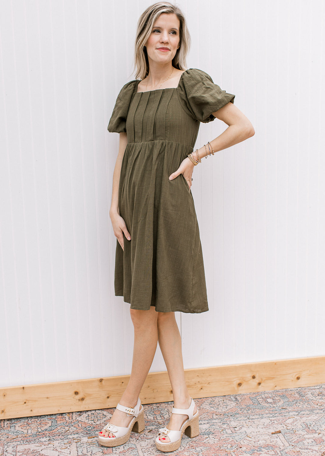 Model wearing heels with a textured olive dress with a square neck and bubble short sleeves.