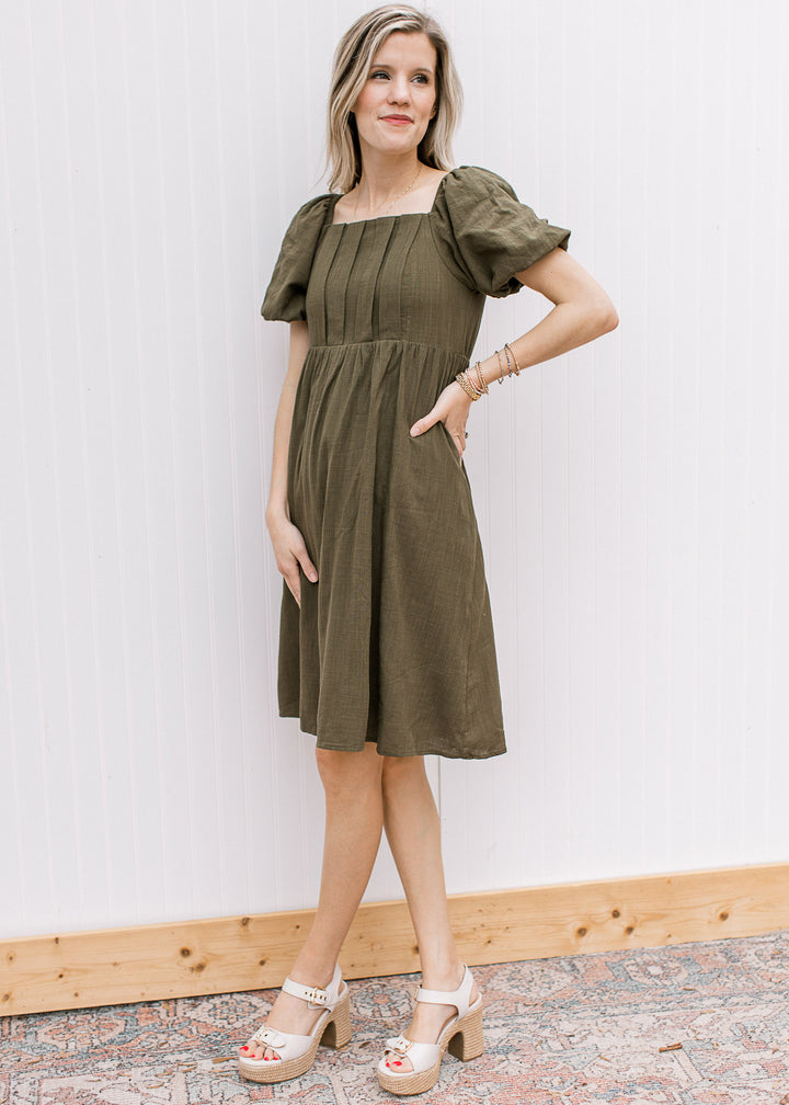 Model wearing heels with a textured olive dress with a square neck and bubble short sleeves.