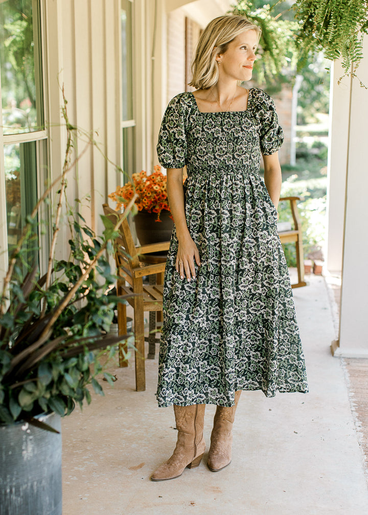 Model wearing boots and an indigo midi with cream and green floral, pockets and short sleeves.