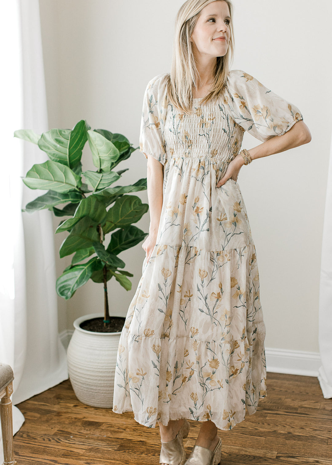 Model wearing a cream midi with gold and steel blue floral, a square neck and smocked bodice. 