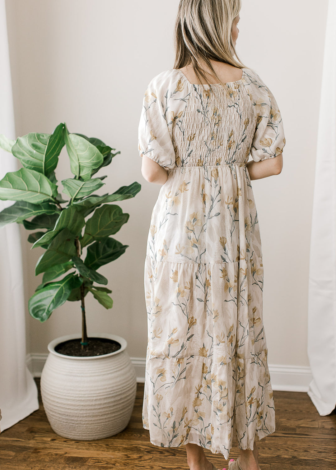 Back view of Model wearing a short sleeve cream midi with floral, a square neck and smocked bodice. 
