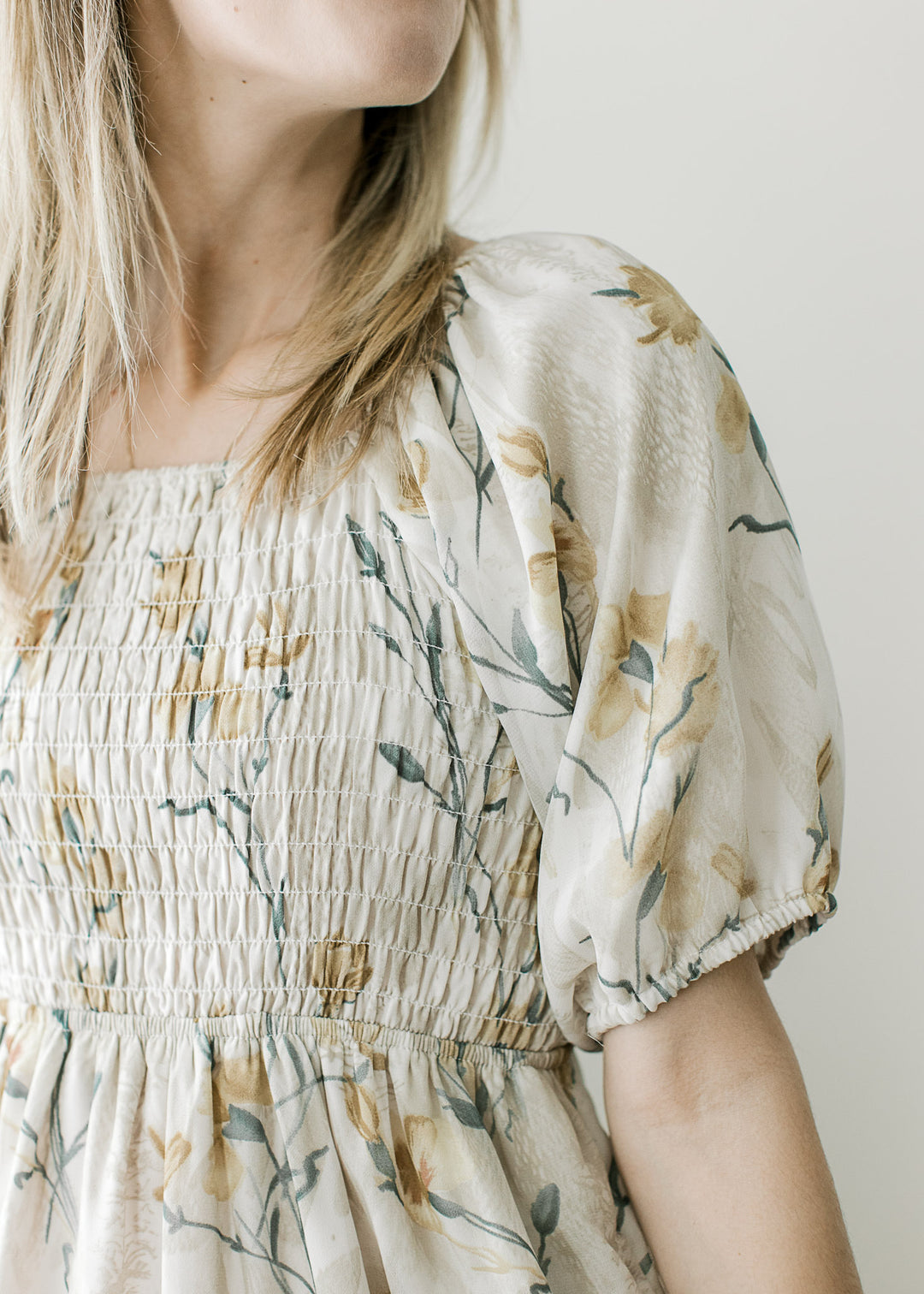 Close up of short sleeve with elastic band on a cream midi with gold and steel blue floral. 