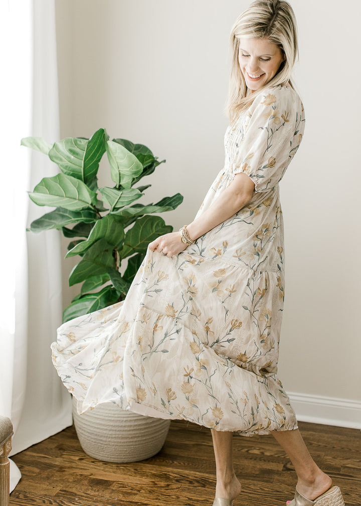 Model twirling in a cream midi with gold and steel blue floral, a square neck and smocked bodice.