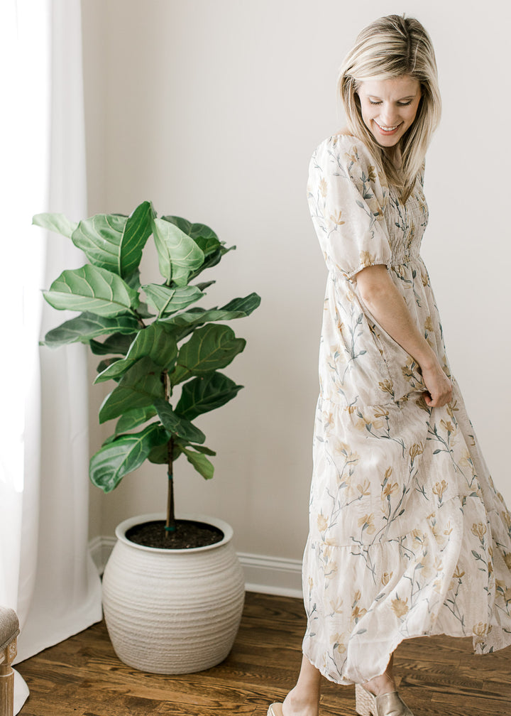 Model wearing a cream midi with floral, a square neck, tiered skirt and smocked bodice.  