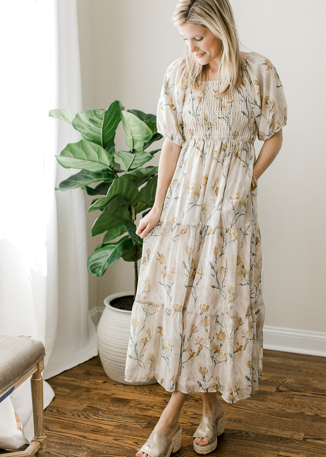 Model wearing heels and a cream midi with floral, a square neck, pockets and smocked bodice. 