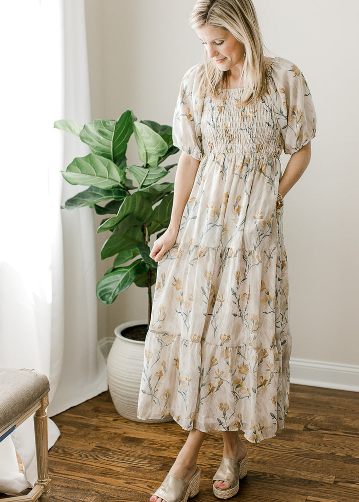 Model wearing heels and a cream midi with floral, a square neck, pockets and smocked bodice. 